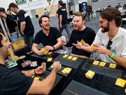 Players laughing while playing Shocking Deal card game at a tabletop convention.
